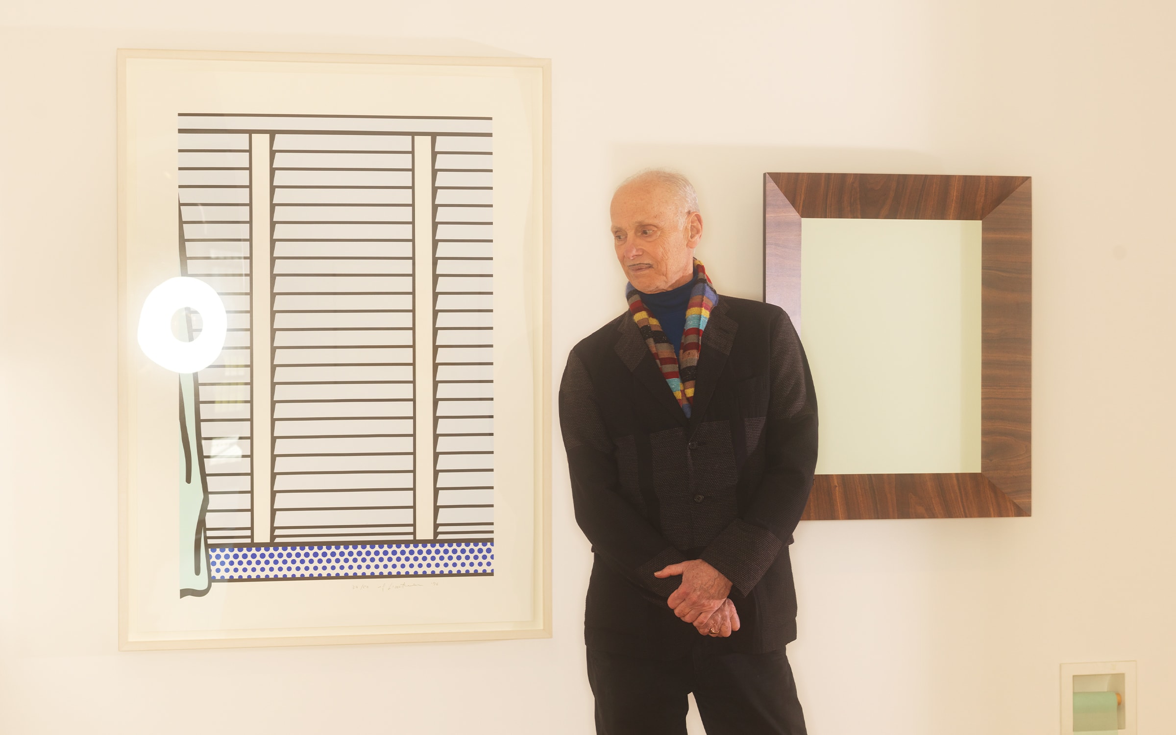 John Waters in his exhibition at the Baltimore Museum of Art, with Roy Lichtenstein's Venetian School II (1996) and Richard Artschwager's Mirror (1988), January 2023. Photograph by Matt Grubb for Art Basel.